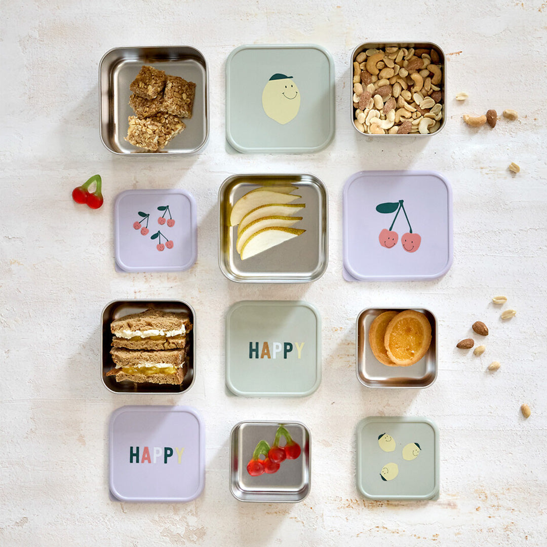 Een bovenaanzicht van diverse lässig rvs snackdoosjes voor kinderen, sommige gevuld met snacks, met deksels met citroen-, kers- en 'HAPPY'-opdruk.