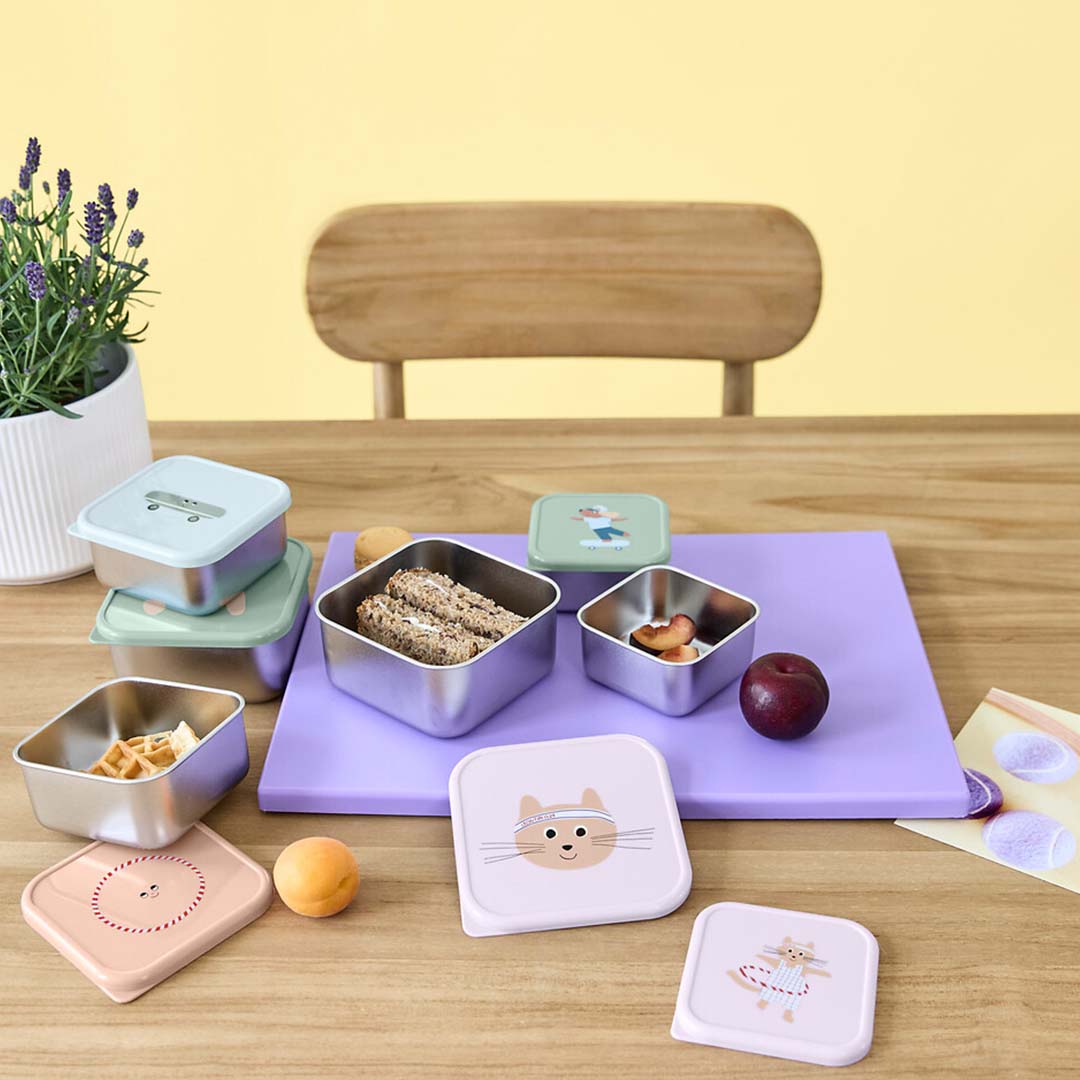 Diverse lässig rvs snackdoosjes voor kinderen met dieren- en figuurthema's op een houten tafel met snacks.