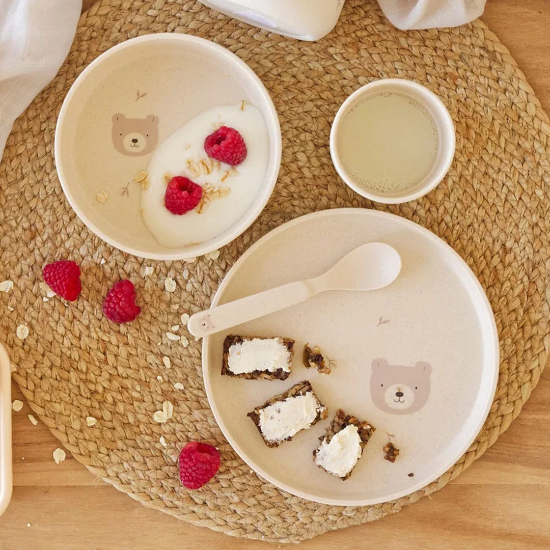 Bovenaanzicht van een Lässig beige babyserviesset met berenpatroon, met een kom gevuld met yoghurt en een bord met een lepel en brood.