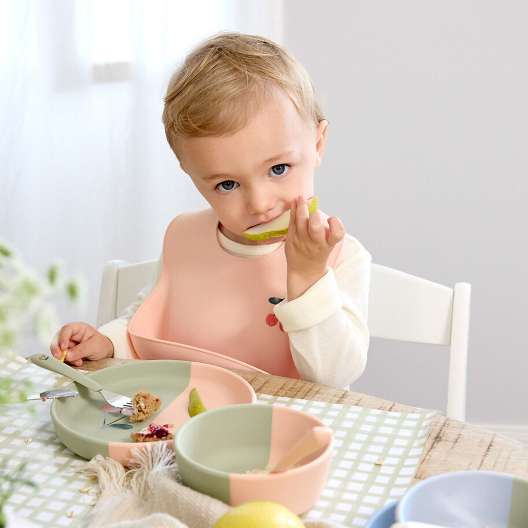Een baby draagt het lässig roze siliconen slabbetje met kersendesign tijdens het eten.