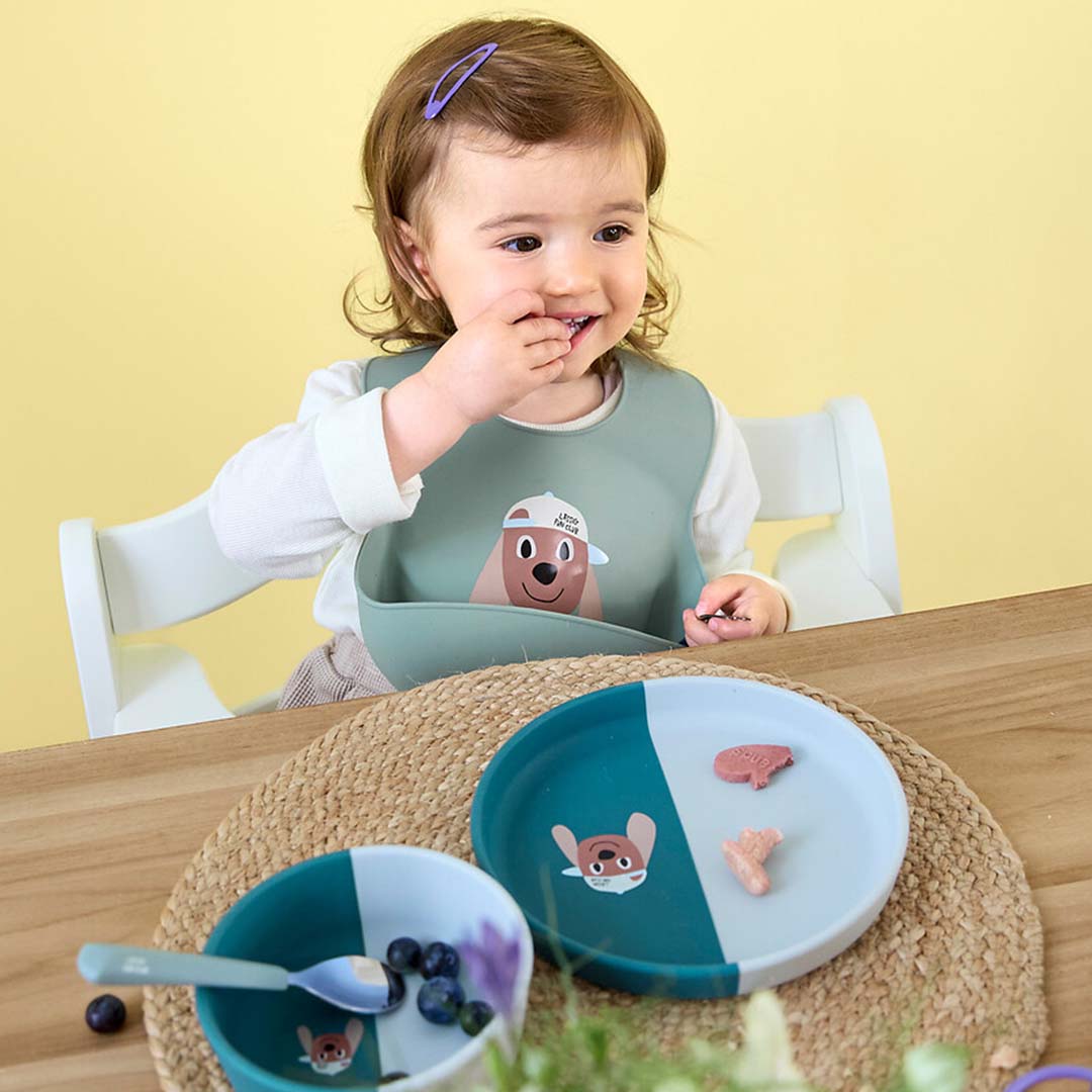 Een baby draagt het Lässig groene siliconen slabbetje met hondenthema tijdens het eten.
