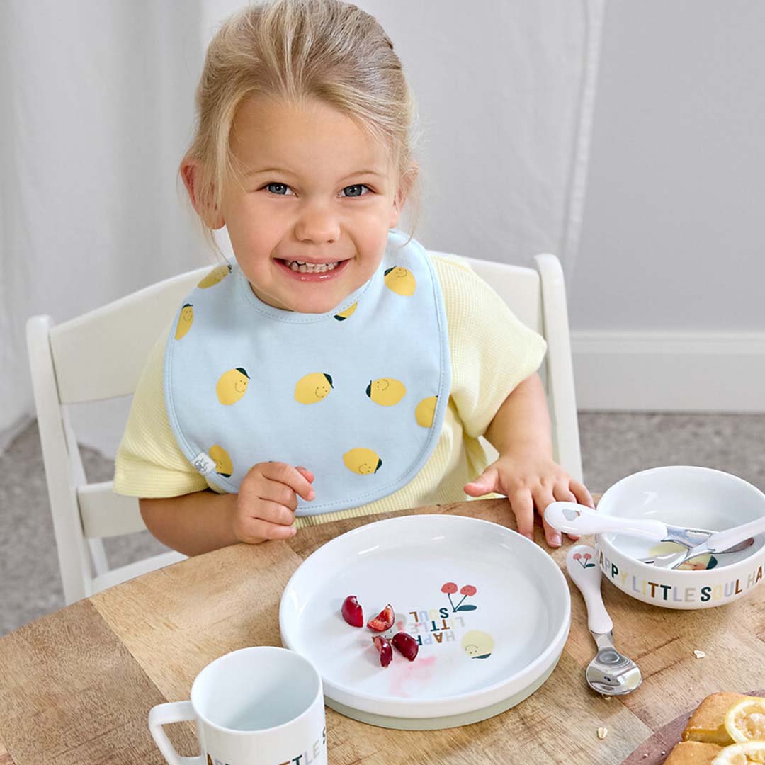 Een lachend kind draagt een lichtblauw baby slabbetje met citroenpatronen tijdens het eten.