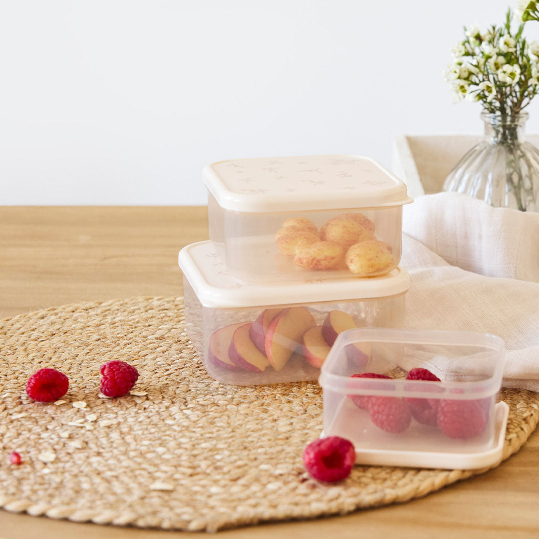Twee gestapelde lässig snackdoosjes voor kinderen met bladeren patroon, gevuld met fruit, op een tafel met een open doosje in de voorgrond.