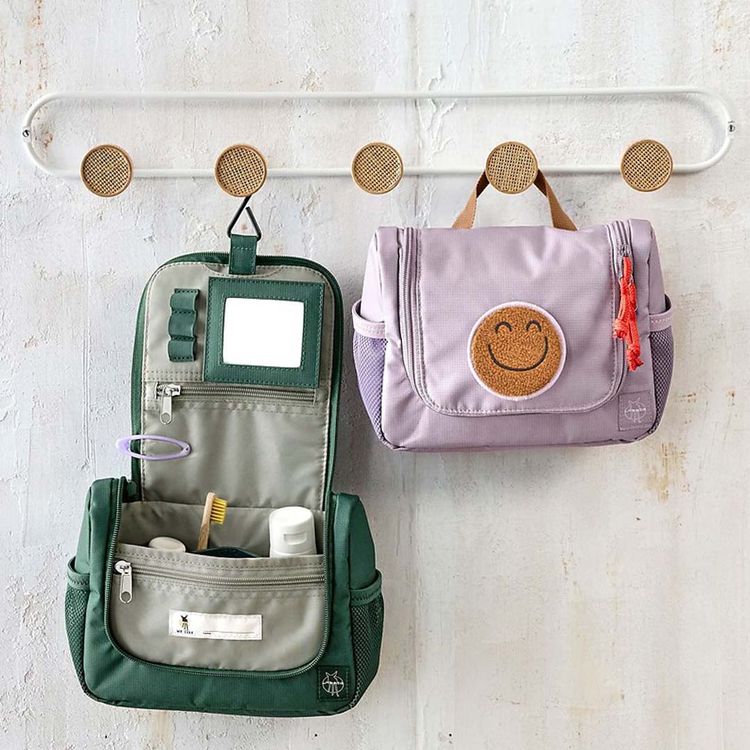 Twee lässig toilettassen, een open groene en een gesloten lila met smiley, hangen aan een kapstok.