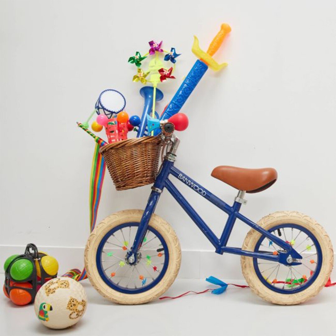 Een blauwe loopfiets met een mand vol speelgoed, waaronder een zwaard en een fietstoeter.