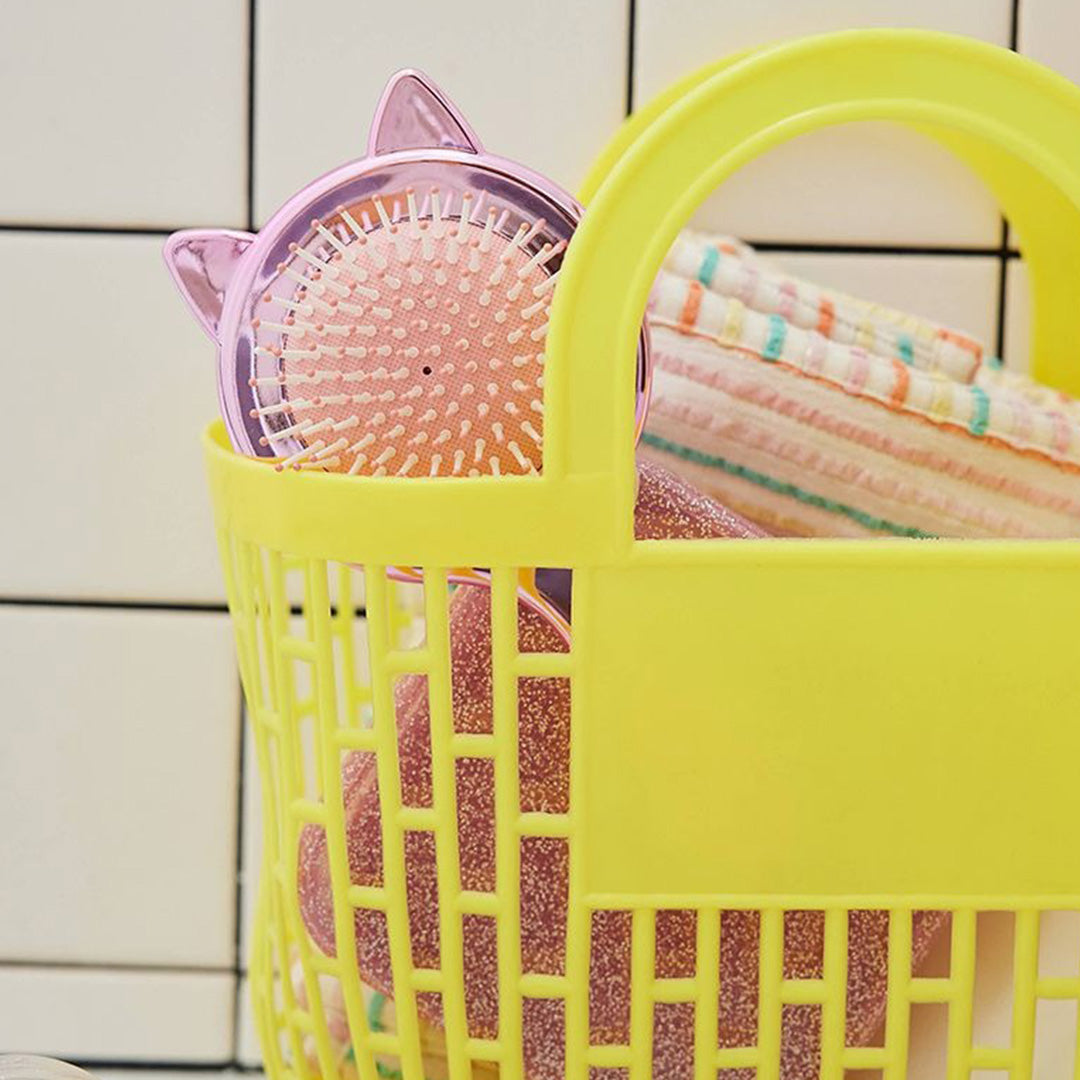 Roze haarborstel met kattenoren steekt uit een gele plastic mand met een handdoek.