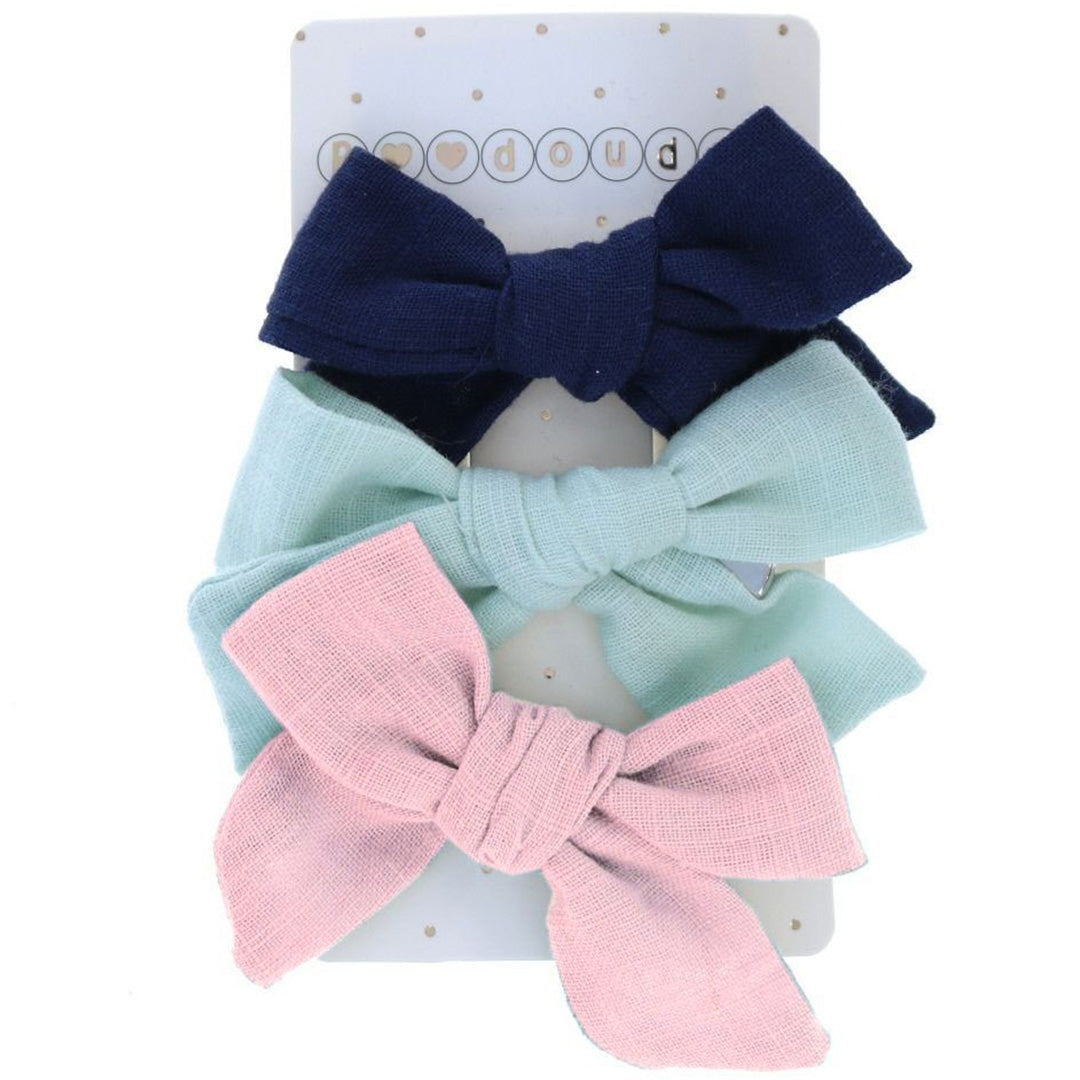 De verpakking van drie le petit souk stoffen haarspeldjes in de vorm van strikjes in donkerblauw, lichtblauw en roze.