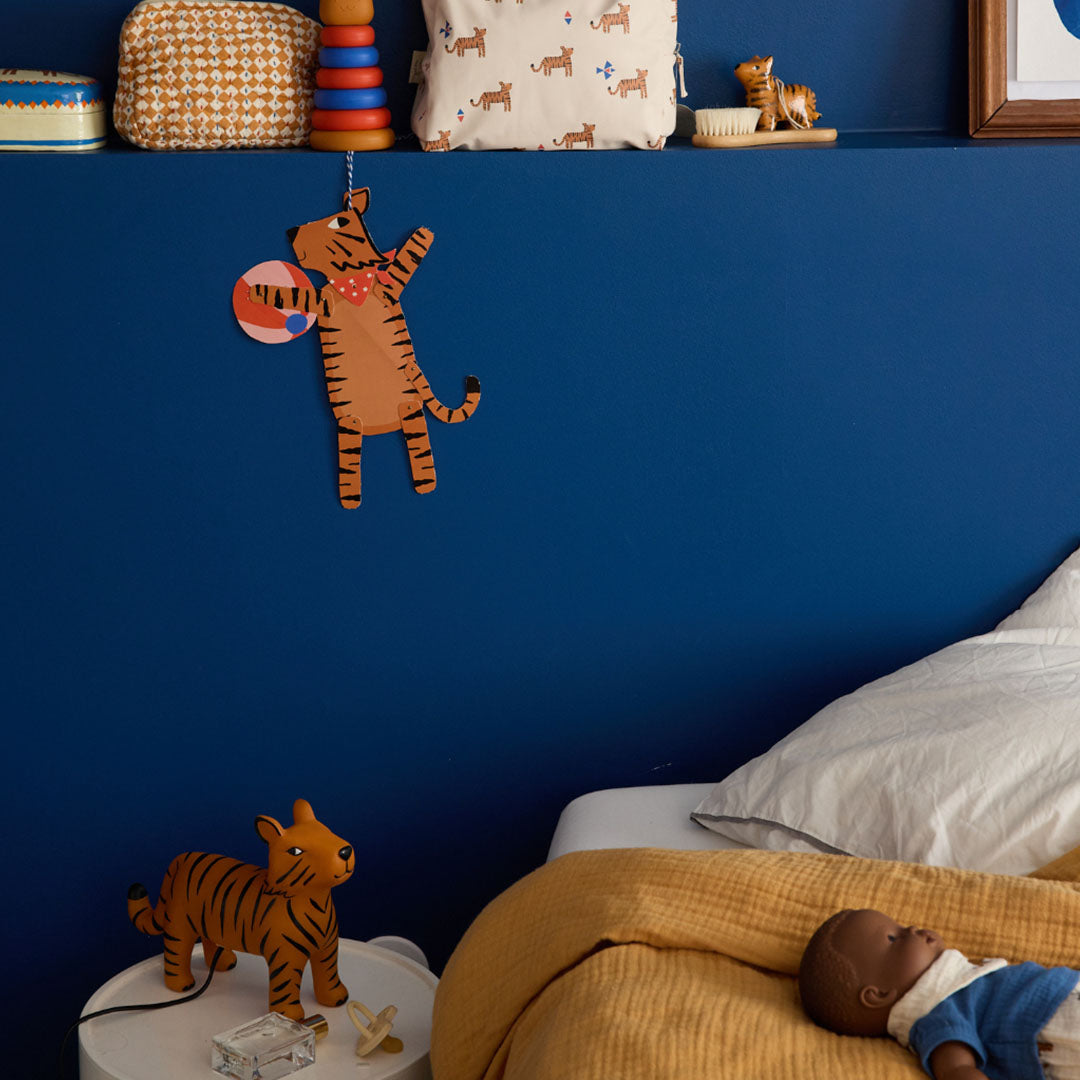 De oranje tijger kinderlamp staat op een nachtkastje in een kinderkamer met blauwe muur.