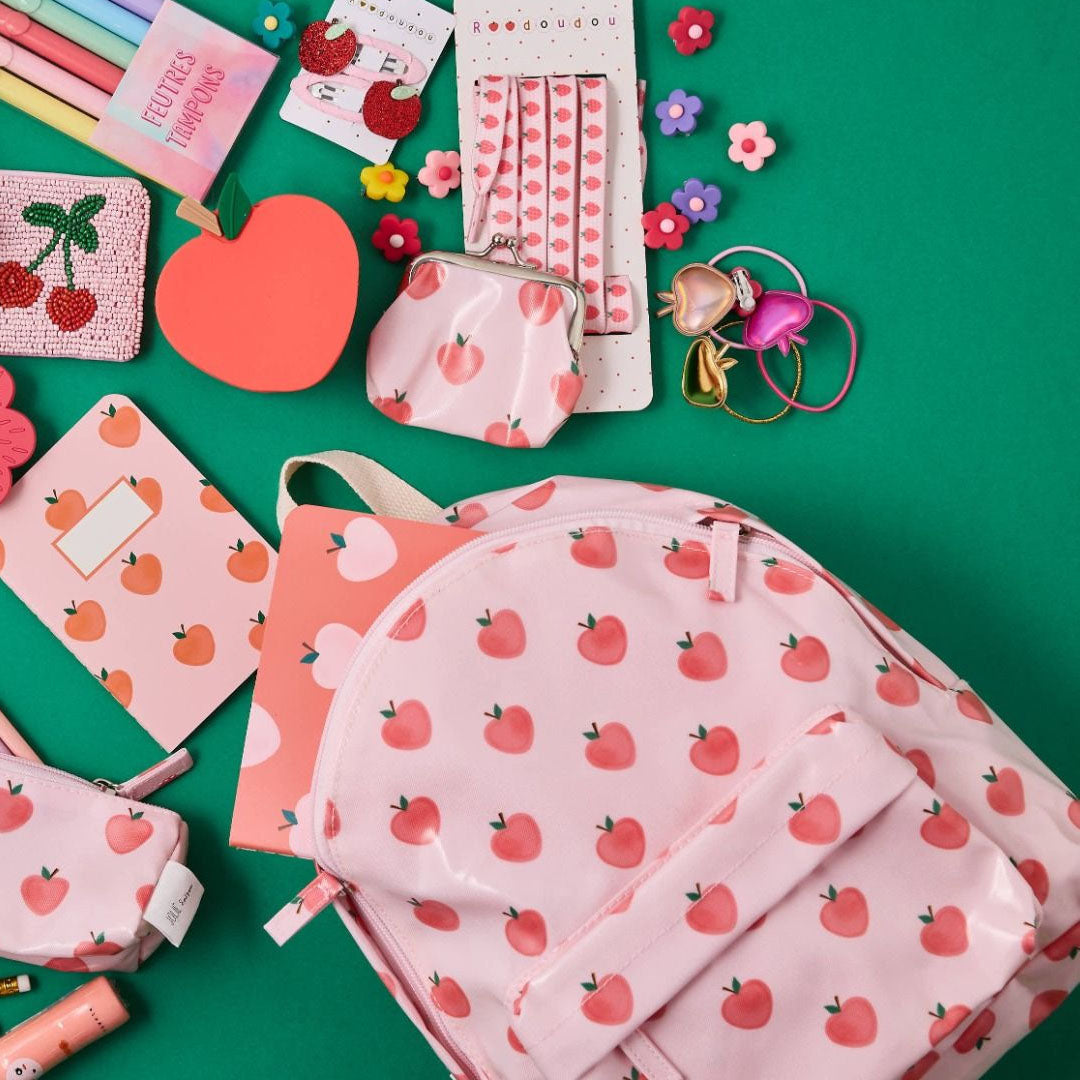 le petit souk kleuterrugzak met appelpatroon, omringd door bijpassende schoolspullen en accessoires op een groene achtergrond.