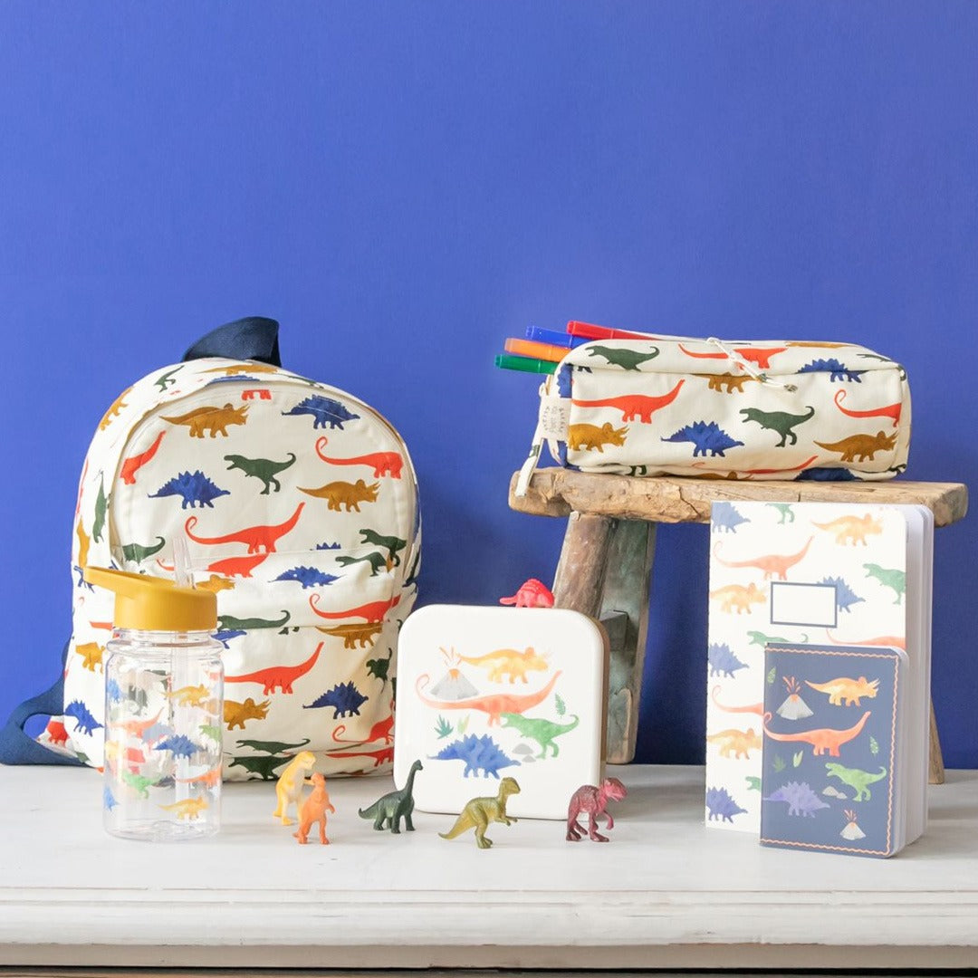 Een collectie le petit souk schoolspullen met dinosauruspatroon, waaronder de kleuterrugzak, op een witte tafel.