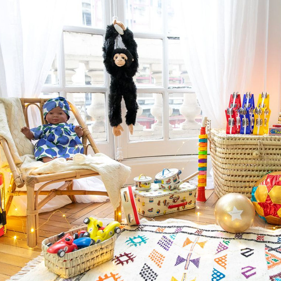 De le petit souk pluchen aap hangt aan een gordijnroede in een kinderkamer met speelgoed.