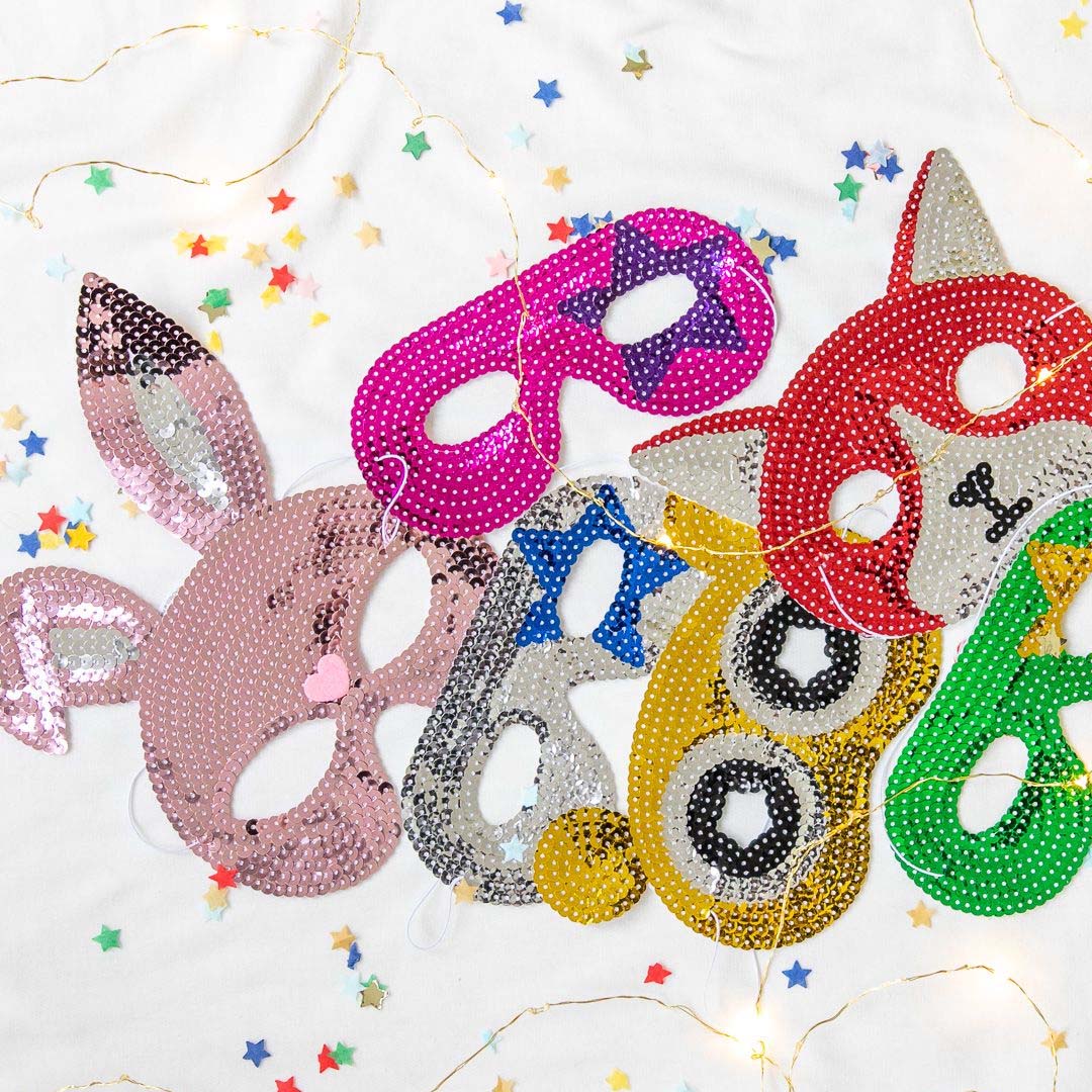 Een collectie van diverse kinder maskers met pailletten, waaronder een roze konijn, een rode vos en een gele uil, liggend op een witte ondergrond met confetti.