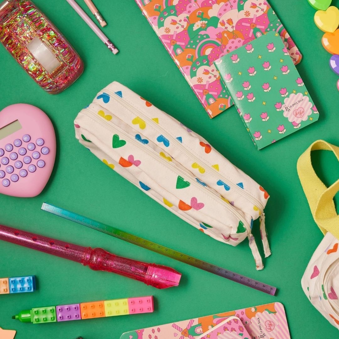 Een bovenaanzicht van diverse roze en groene kantoorartikelen, waaronder een le petit souk plakbandhouder met glitters.