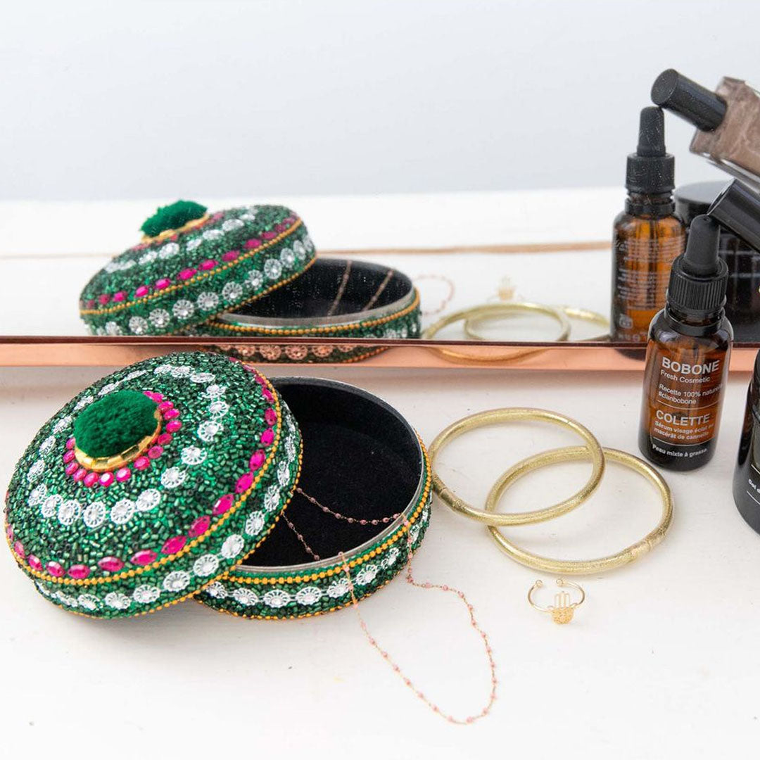 Le petit souk groen sieradendoosje met pompom, open met sieraden en cosmetica op een tafel.