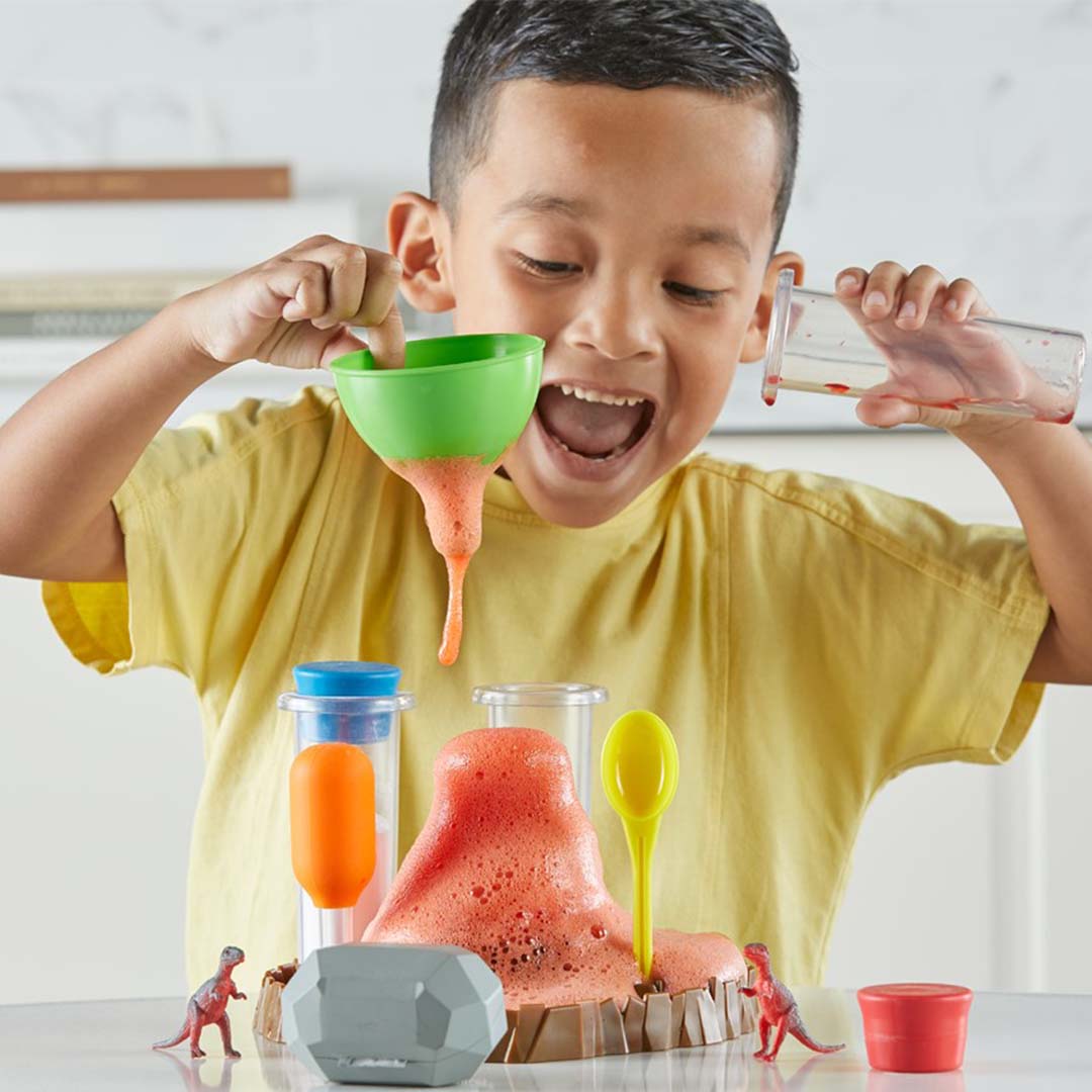 Een kind giet vloeistof in een trechter, waardoor een oranje schuimende vulkaanuitbarsting ontstaat met de Fizzy Volcano wetenschapsset.