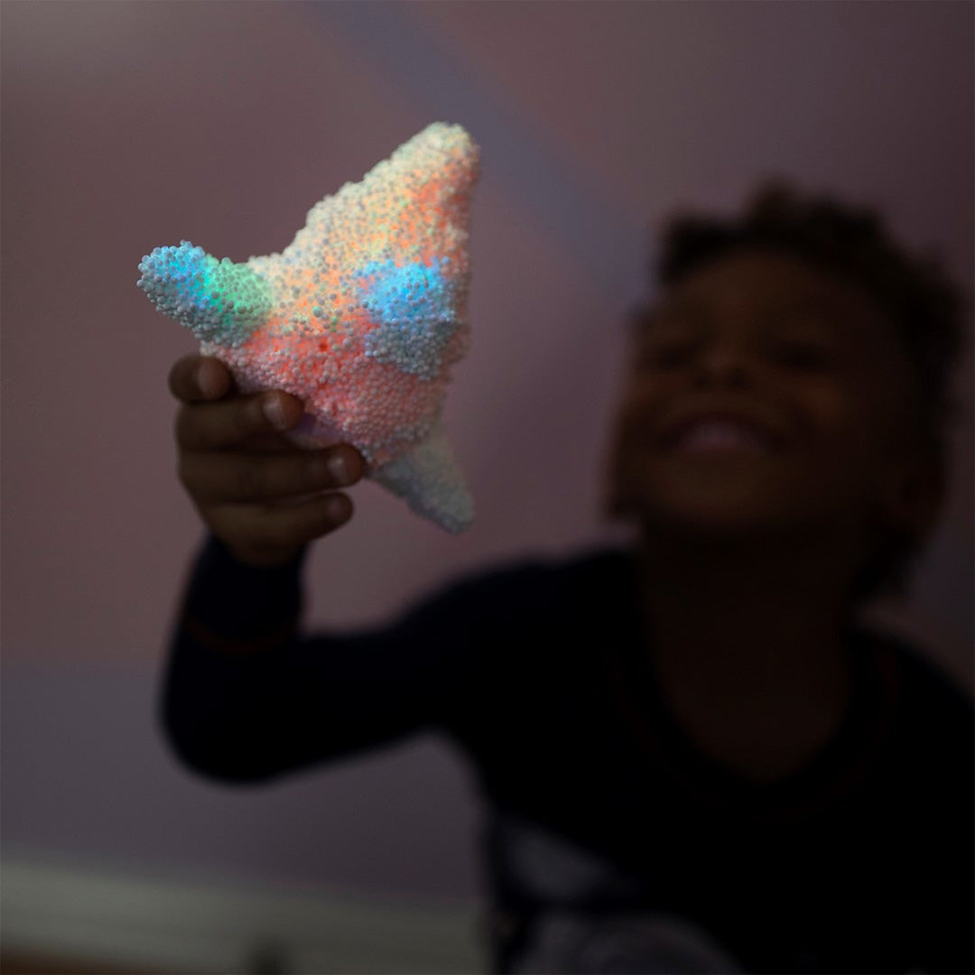 Een kind houdt een oplichtend Playfoam raketfiguur vast dat roze, blauw en groen gloeit in het donker.
