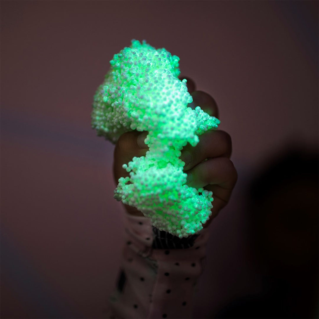 Een hand knijpt in een klompje felgroene, glow-in-the-dark Playfoam in het donker.