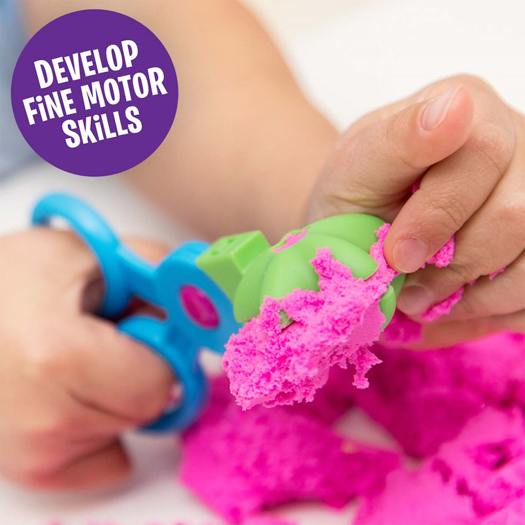 Kinderhanden gebruiken een blauwe schaar om roze Playfoam Sand te knippen.