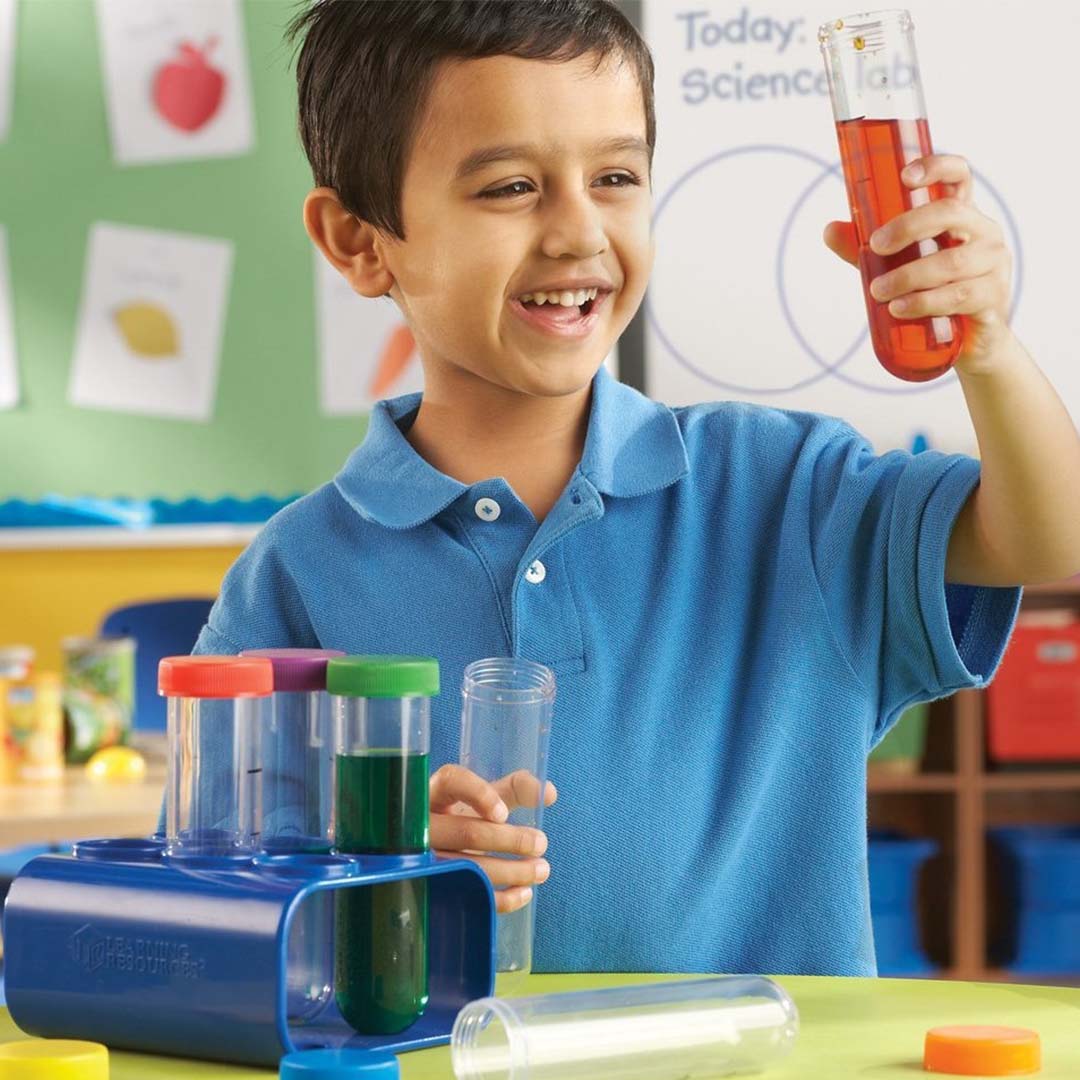 Een lachend kind houdt een Learning Resources jumbo reageerbuisje met oranje vloeistof vast.