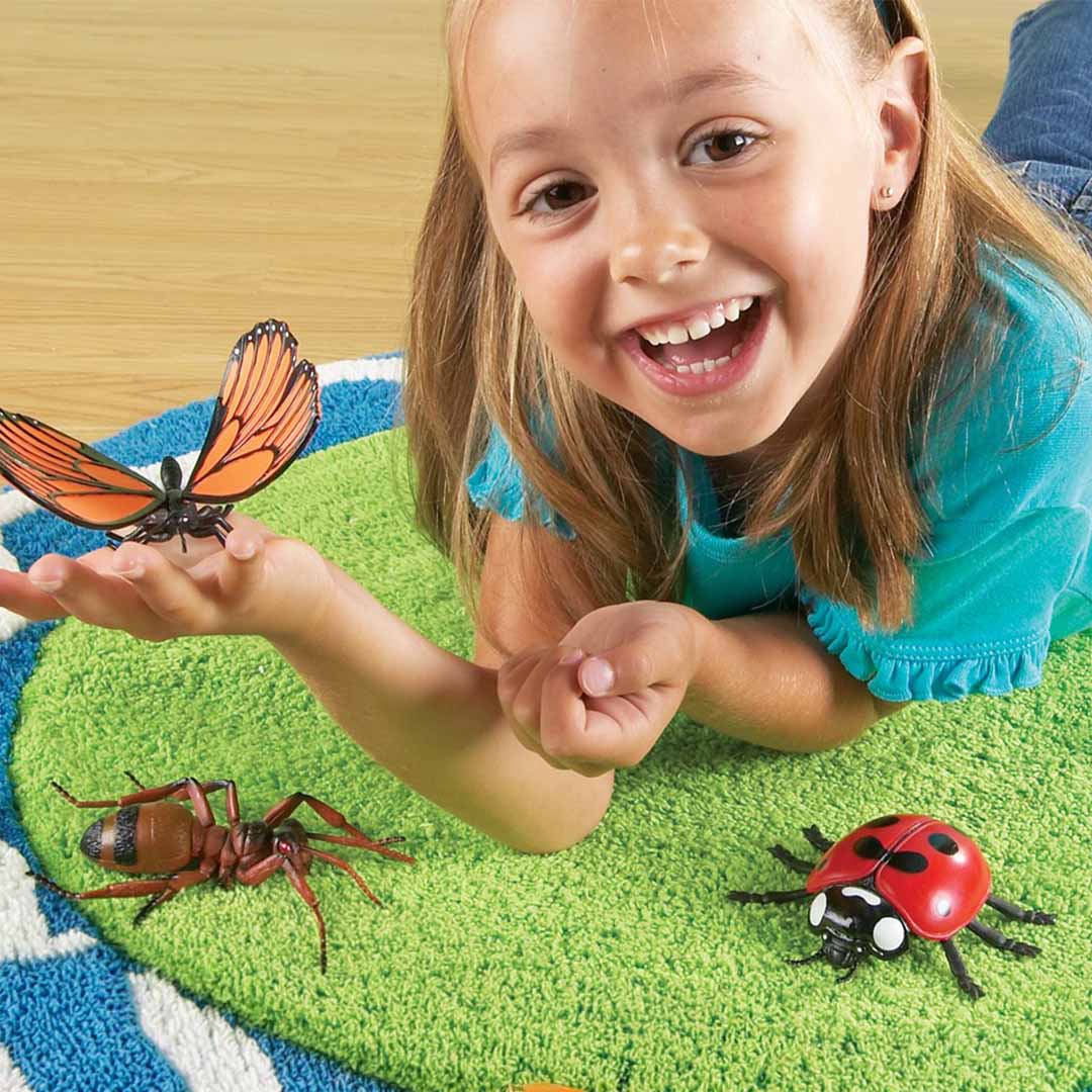 Een lachend meisje speelt met een Learning Resources Jumbo Insects vlinderfiguur en andere insectenfiguren.