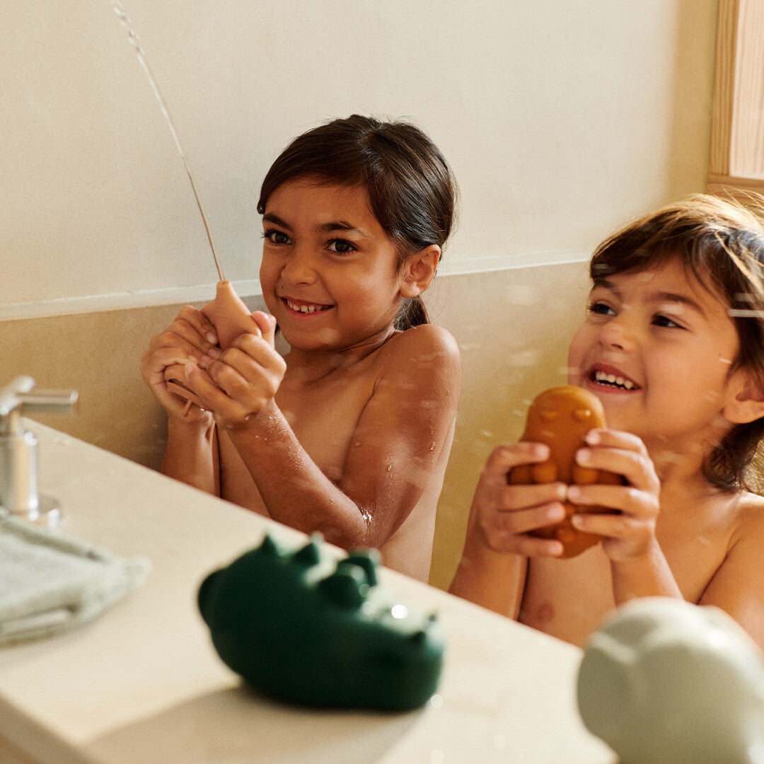 Twee lachende kinderen spelen in bad met Liewood badspuiters.