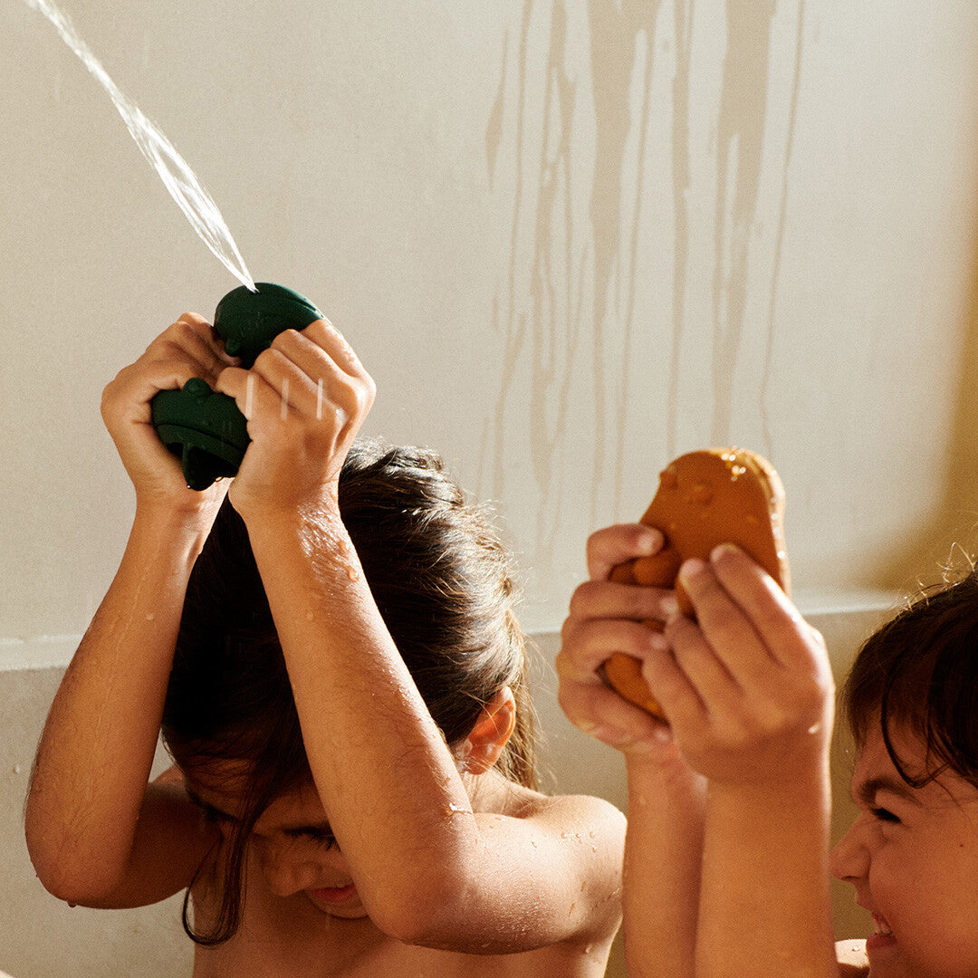 Twee kinderen spuiten water in bad met Liewood badspuiters.