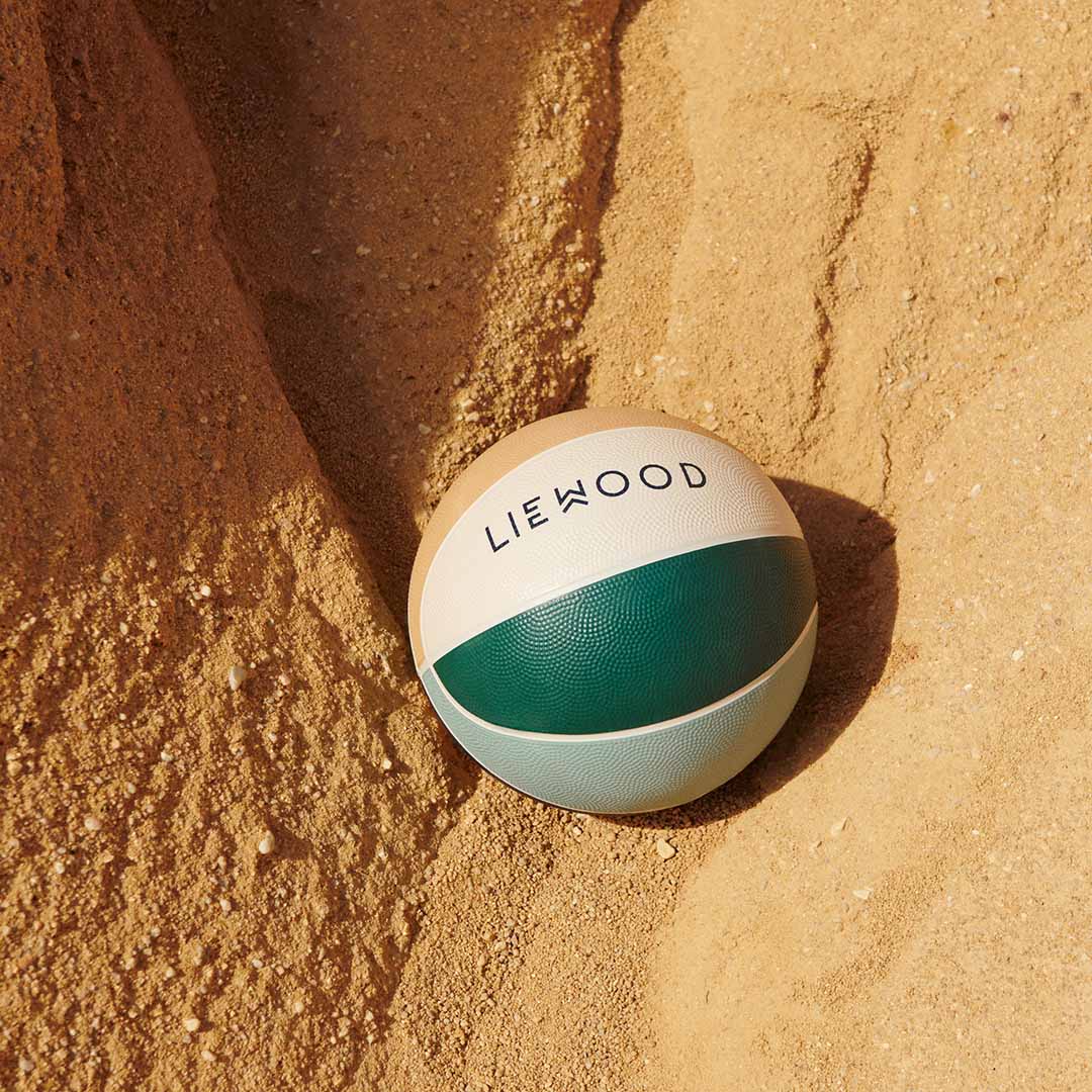 Liewood Desmond basketbal in beige, groene en blauwe kleuren, liggend in het zand.