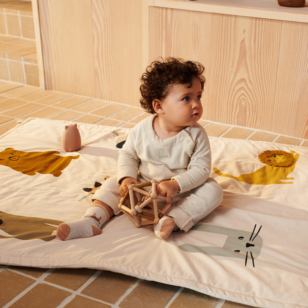 Een baby zit op een speelkleed met dieren en houdt het Liewood grijpspeeltje Annemette vast.
