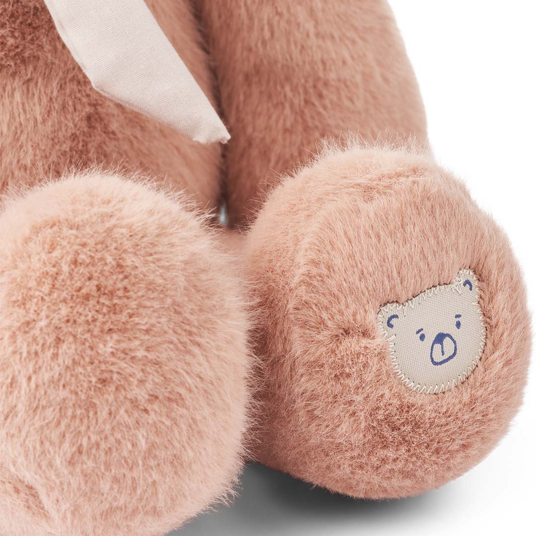 Detail van de voet van een roze pluchen knuffelkonijn met een geborduurd berenlogo.