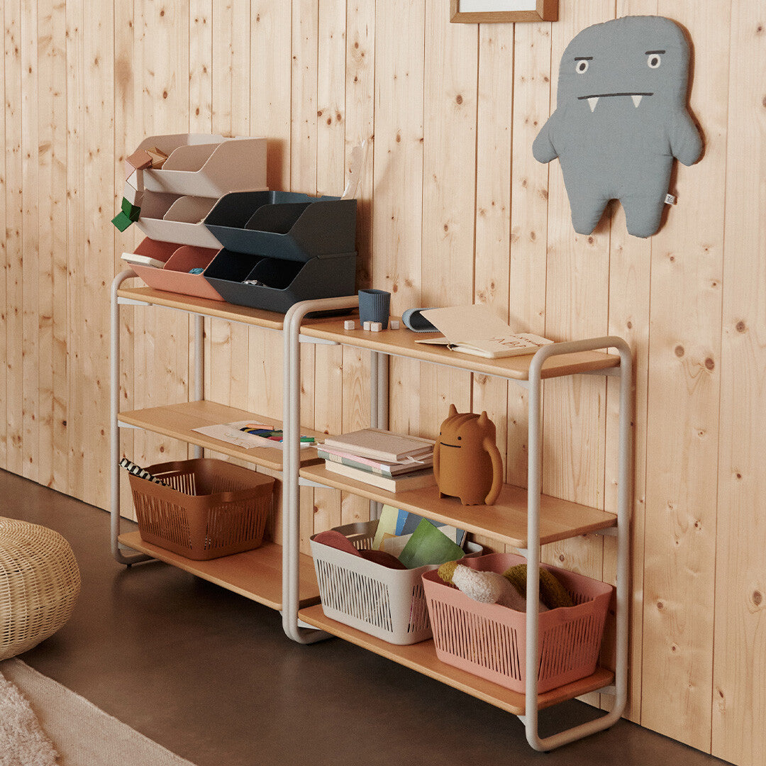 Liewood opbergbakken en andere opbergers op een houten rek in een kamer met houten wanden.