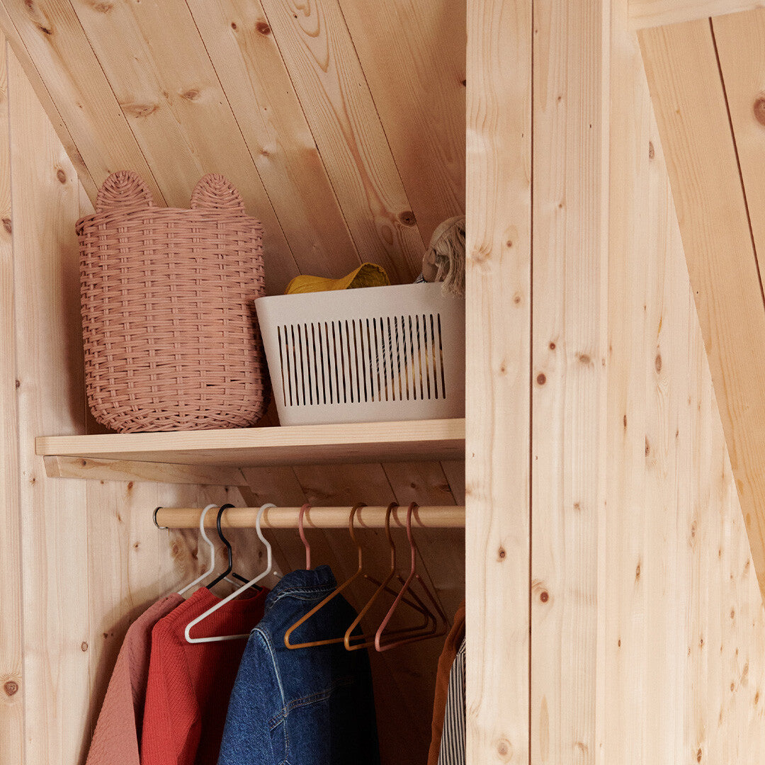 Een beige Liewood opbergbak staat op een houten plank in een kast, naast een roze mand.