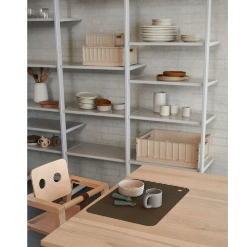Een kinderstoel en eettafel met op de achtergrond beige Liewood opbergkratten op planken.