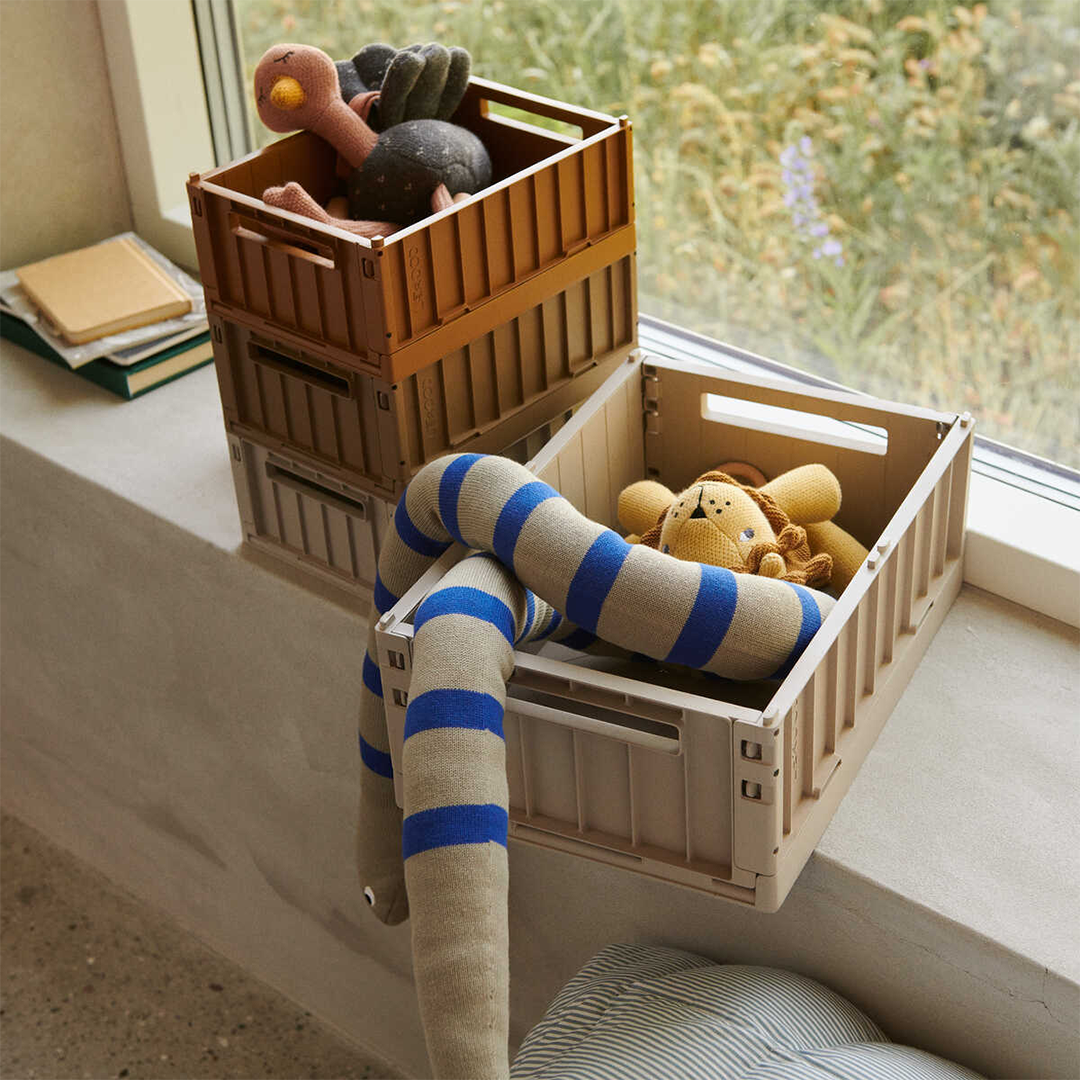Twee Liewood opbergkratten in beige en bruin, gevuld met knuffels, staand op een vensterbank.