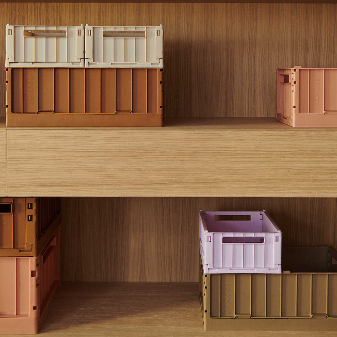 Diverse Liewood opbergkratten in verschillende kleuren staan op houten planken.
