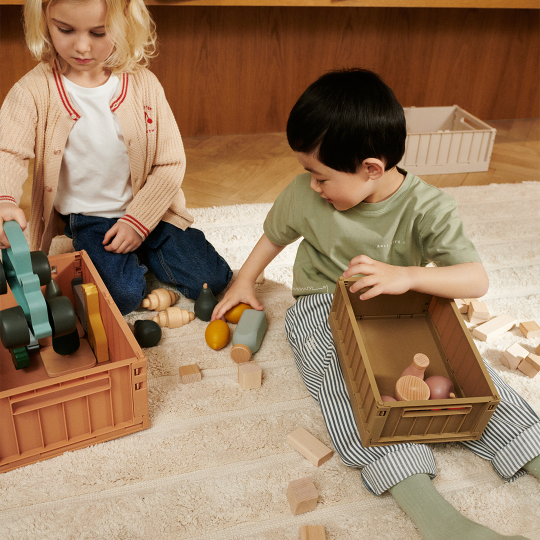 Twee kinderen spelen op een vloerkleed met Liewood opbergkratten en houten speelgoed.