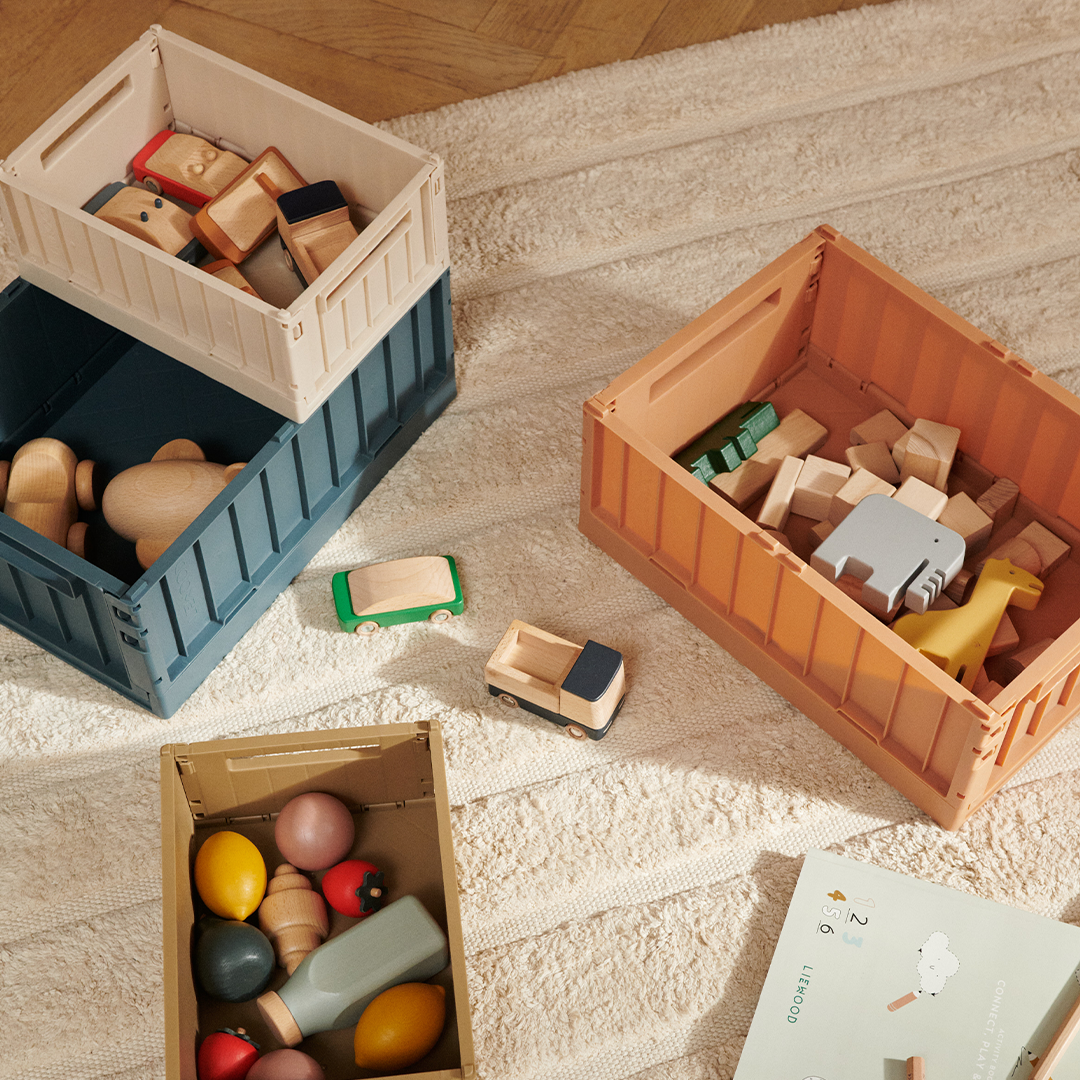 Meerdere Liewood opbergkratten in diverse kleuren, gevuld met houten speelgoed.