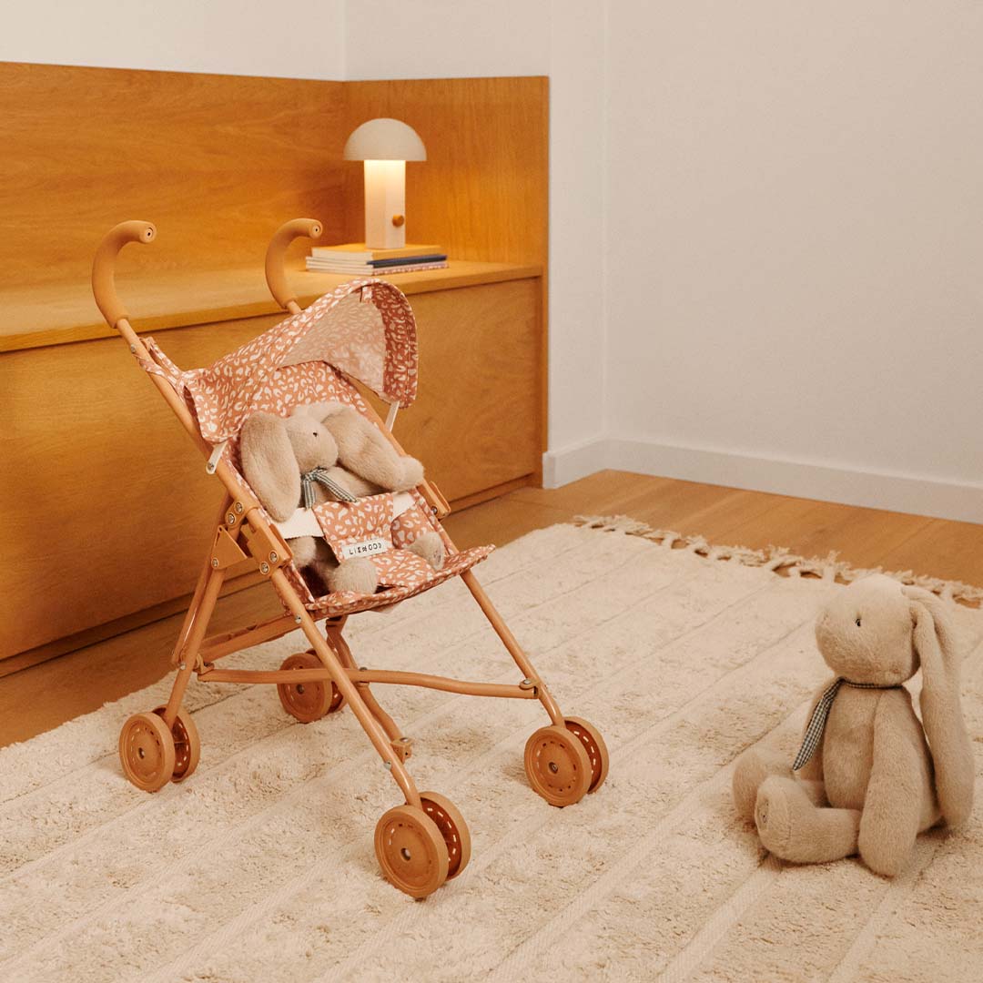 Liewood poppenbuggy Elsie met een pluche konijn erin, staand op een vloerkleed in een kamer.