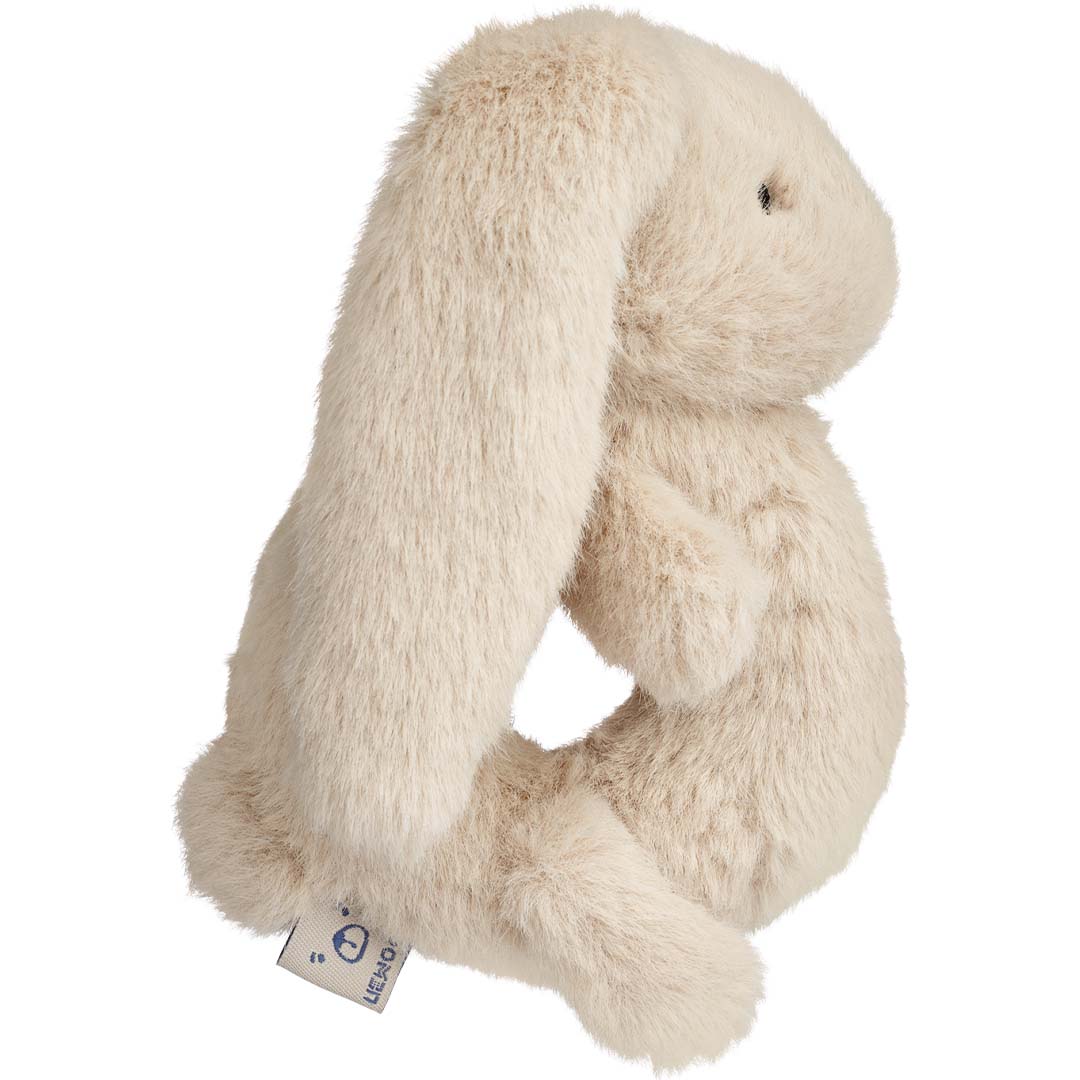Liewood beige pluche konijn rammelaar, schuin van opzij gefotografeerd.