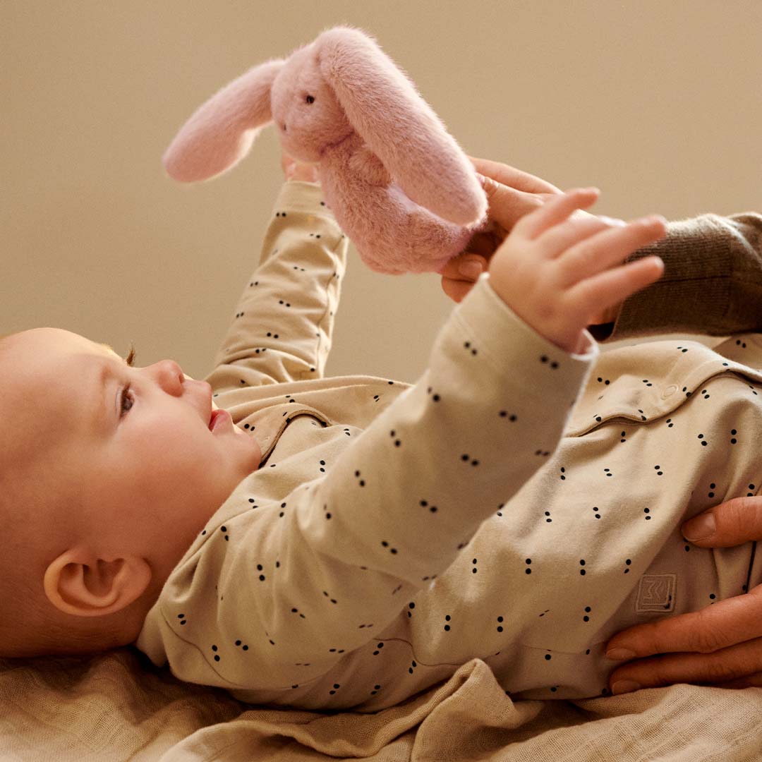 Een baby speelt met een roze pluche konijn rammelaar.