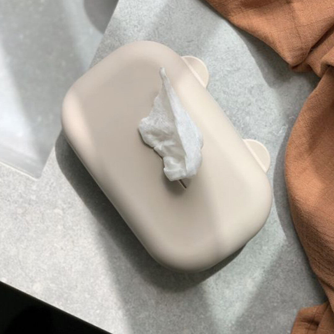 De Liewood siliconen babydoekjes hoes in zandkleur met een doekje dat eruit steekt, op een grijze ondergrond.