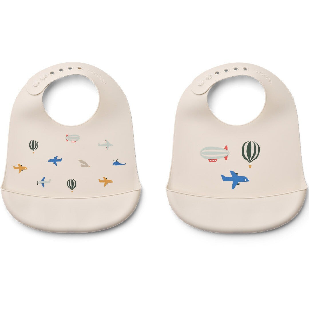 Twee Liewood siliconen slabbetjes voor baby's in ecru met verschillende voertuigpatronen.