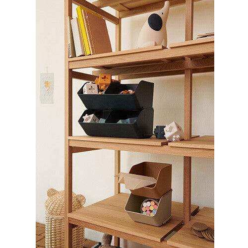 Twee Liewood stapelbare opbergbakken in donkergrijs en bruin, gevuld met speelgoed, op een houten plank.