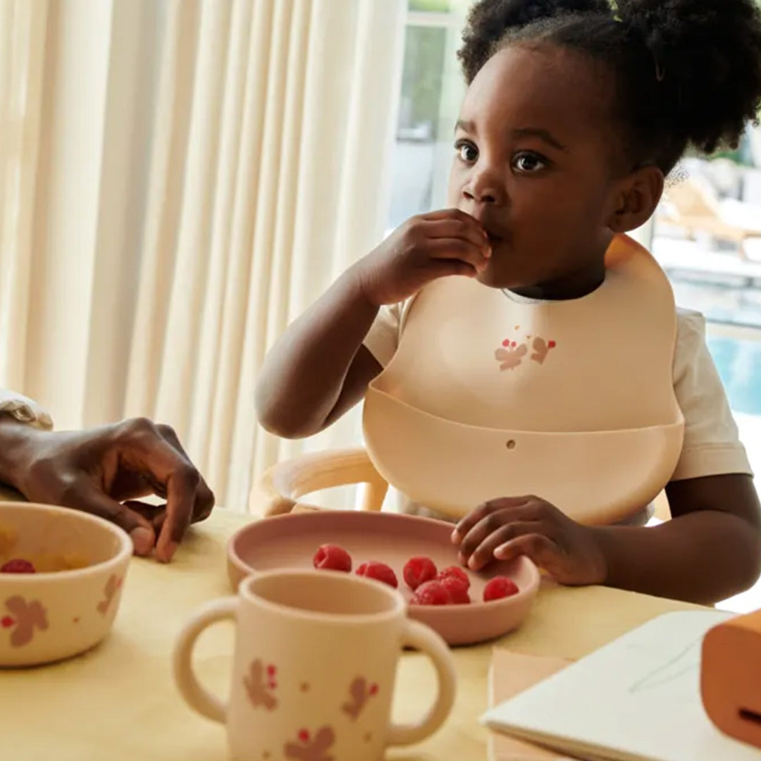 Een kind met een Liewood siliconen slab met vlinderpatroon eet frambozen van het bijpassende kinderservies.