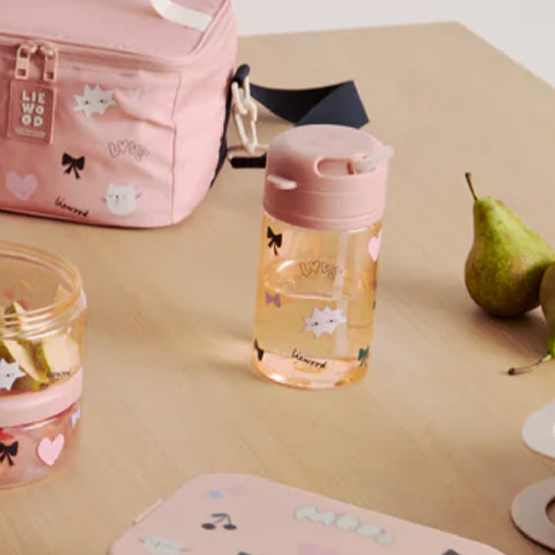 Liewood drinkbeker met rietje op een houten tafel, naast een bijpassende lunchtas en snackbox.