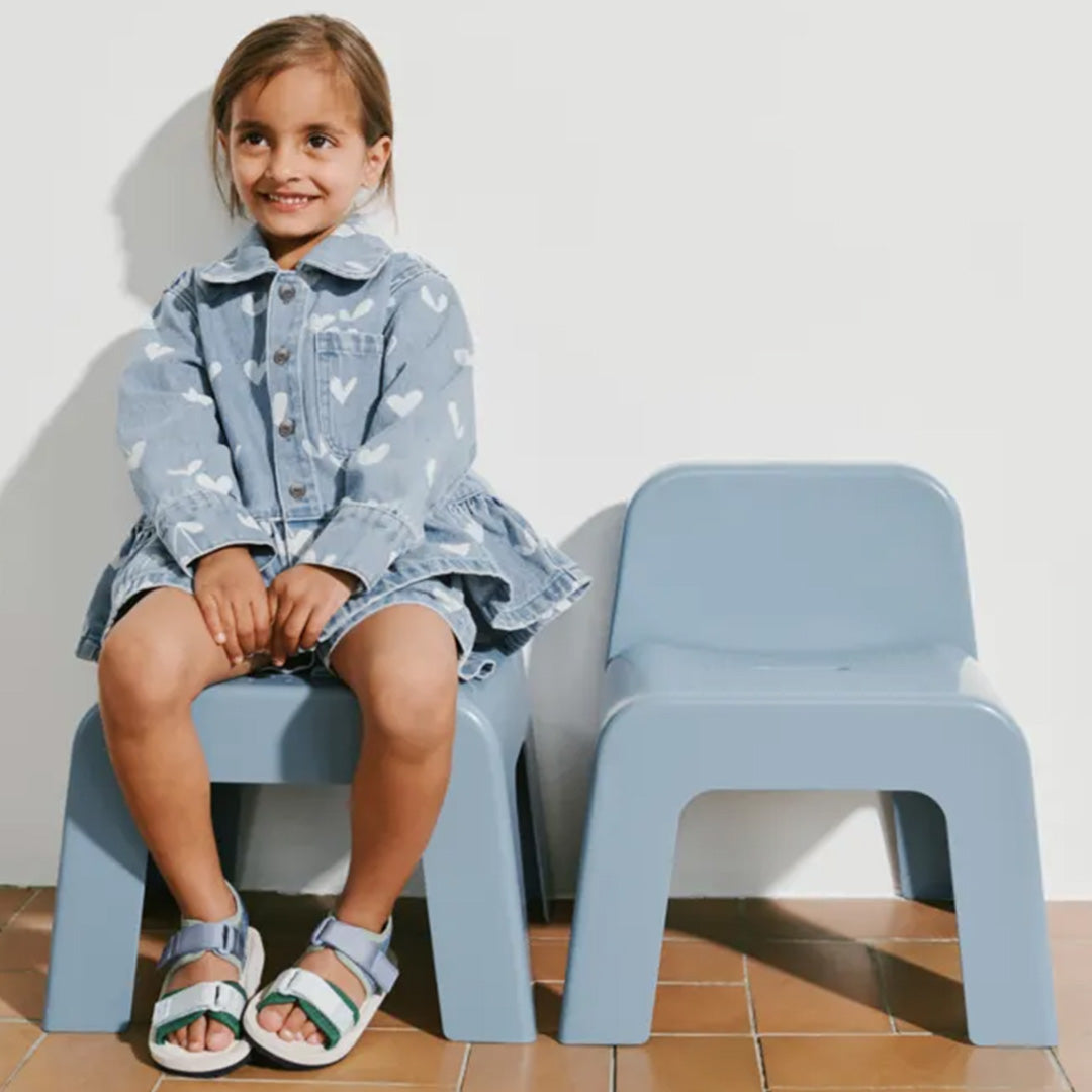 Een meisje zit op een Liewood kinderstoeltje Chase in beach blue, met een tweede stoeltje ernaast.