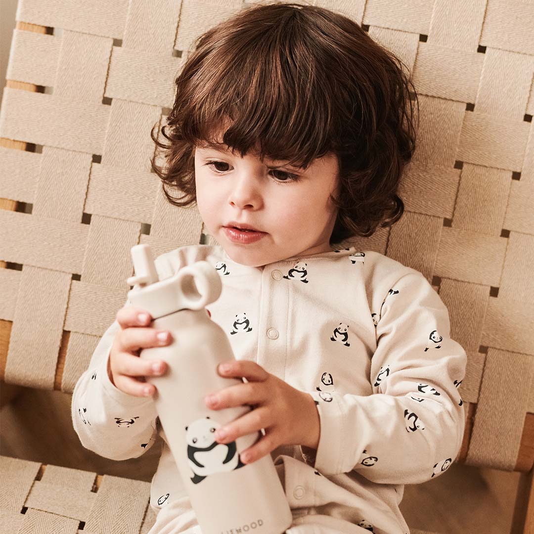 Een kind in een pandapyjama houdt een Liewood kinder waterfles met pandapatroon vast.