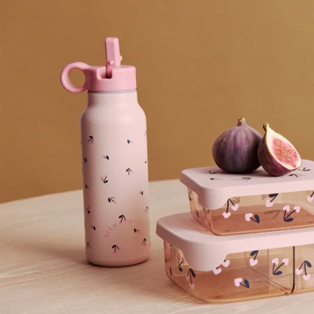 Liewood roze thermosfles met kersenhartjespatroon naast twee bijpassende lunchboxen en vijgen op een tafel.