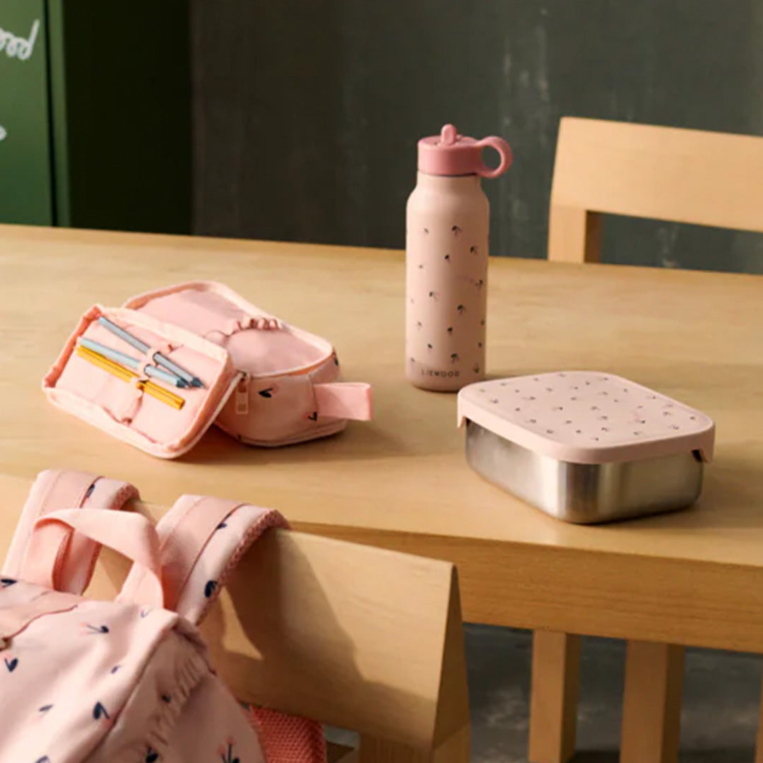 Liewood roze thermosfles met kersenhartjespatroon op een houten tafel naast een etui, rugzak en metalen lunchbox.