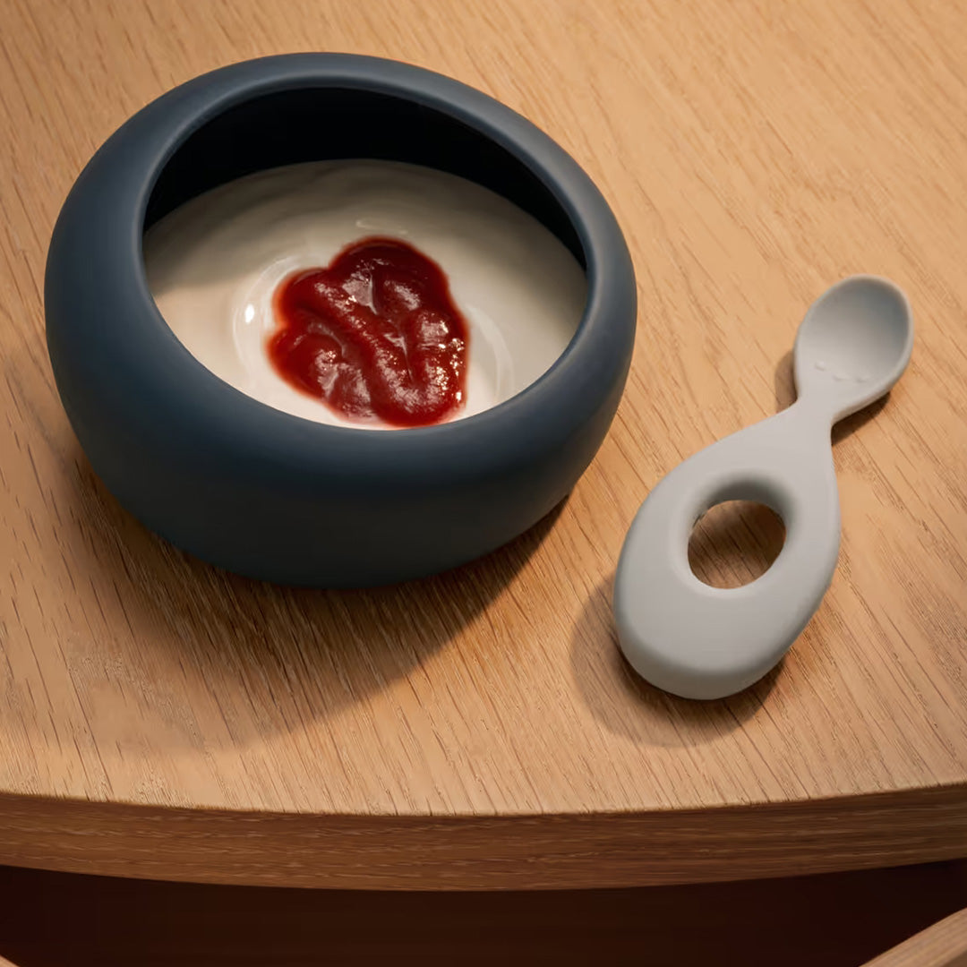Liewood siliconen kinderkom met lepel gevuld met eten op een houten ondergrond.
