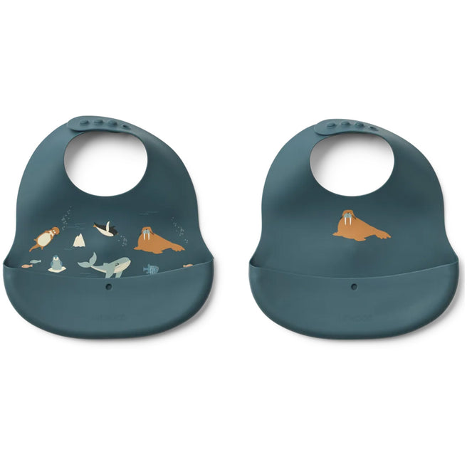 Twee Liewood siliconen slabbetjes in blauw, één met een oceaan thema en één met een walrus.
